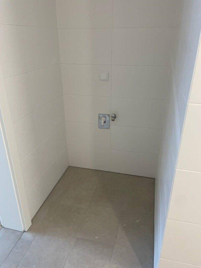 Gefliester Bereich im Badezimmer mit Anschlüssen, bereit für die Installation einer Dusche oder Waschmaschine.