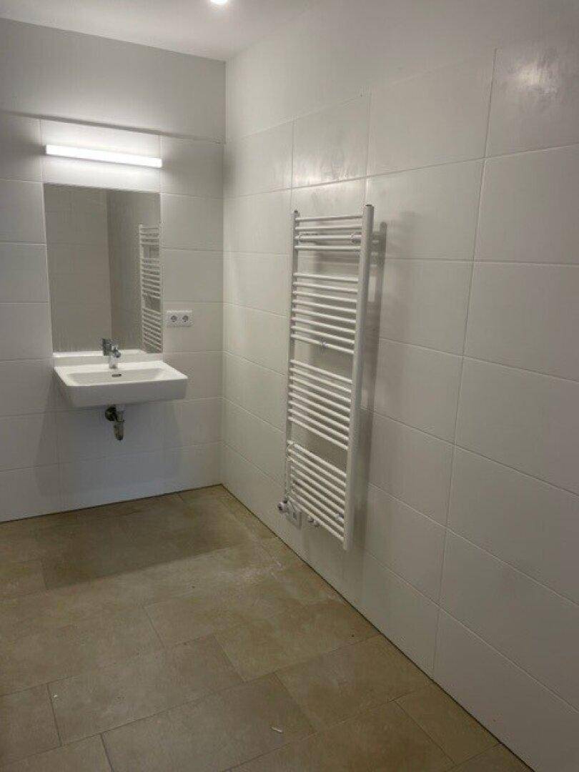 Helles Badezimmer mit Waschbecken, Spiegel und Handtuchheizkörper, komplett gefliest in Weiß.