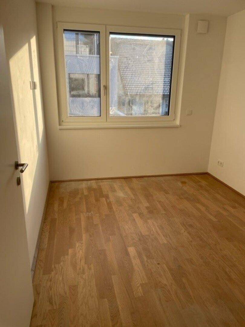 Helles Zimmer mit Parkettboden und großem Fenster, das viel natürliches Licht hereinlässt.