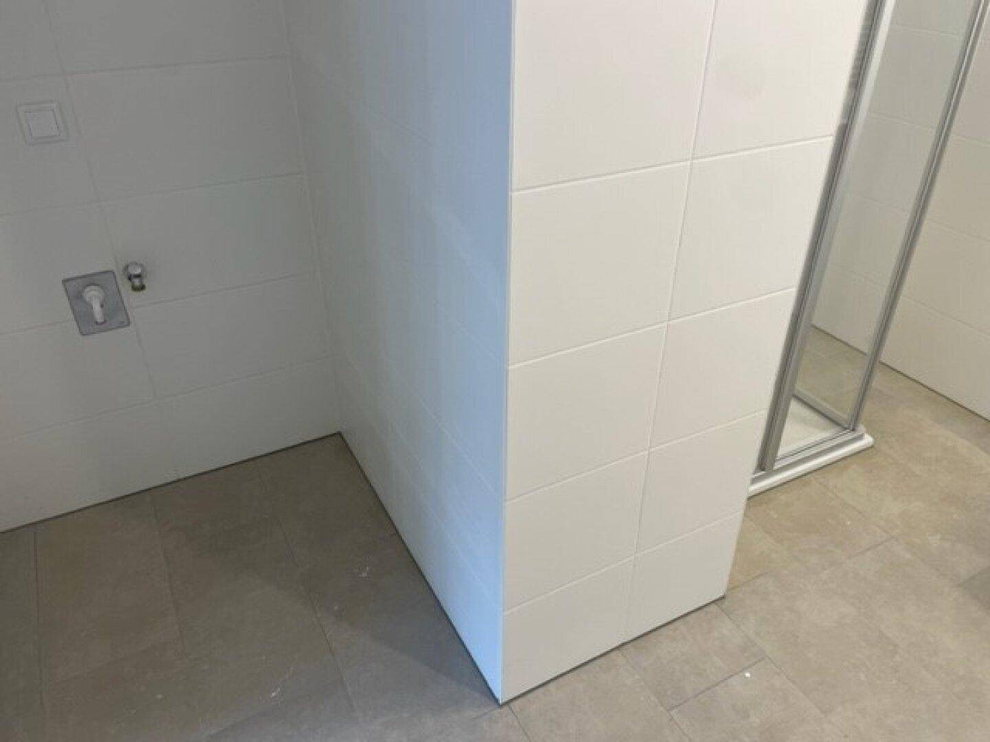 Sauber geflieste Wand im Badezimmer, die den Bereich der Duschkabine abgrenzt.