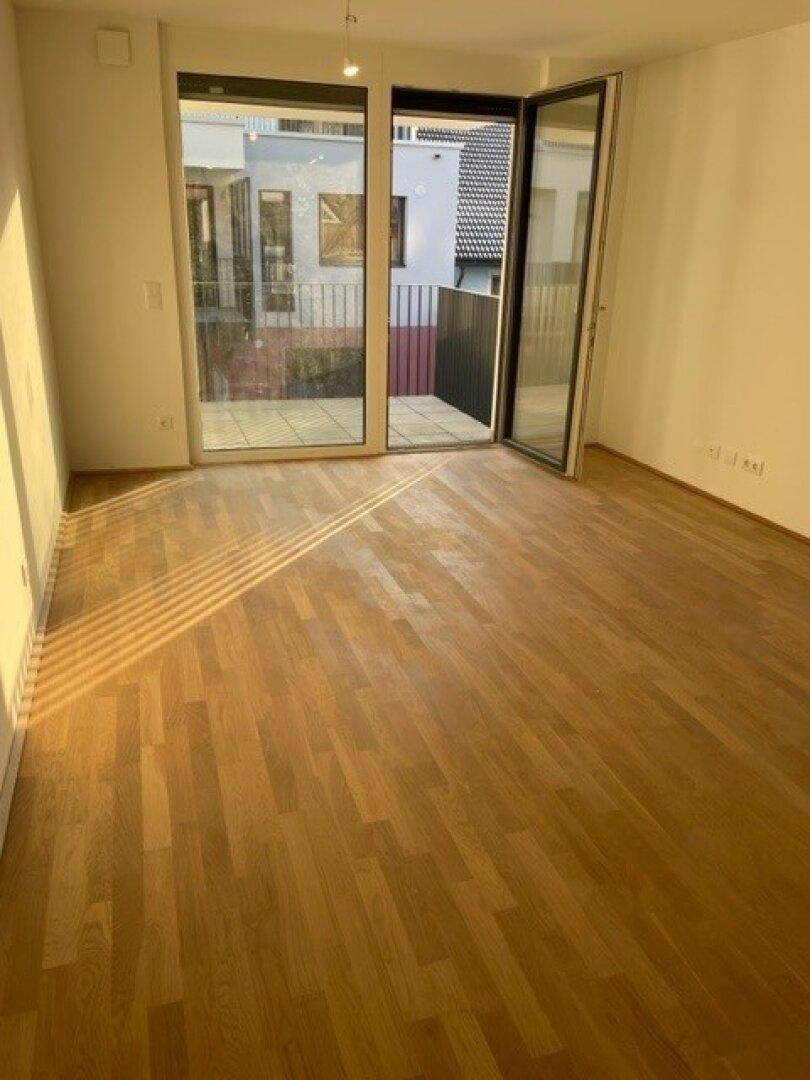 Heller Raum mit Parkettboden und Zugang zu einem Balkon, der viel Tageslicht hereinlässt.