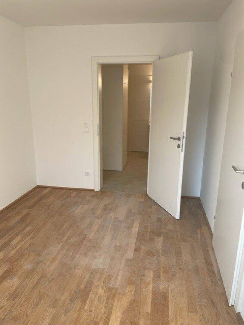 Geräumiges Zimmer mit Parkettboden und Zugang zu einem Flur, der weitere Räume erschließt.