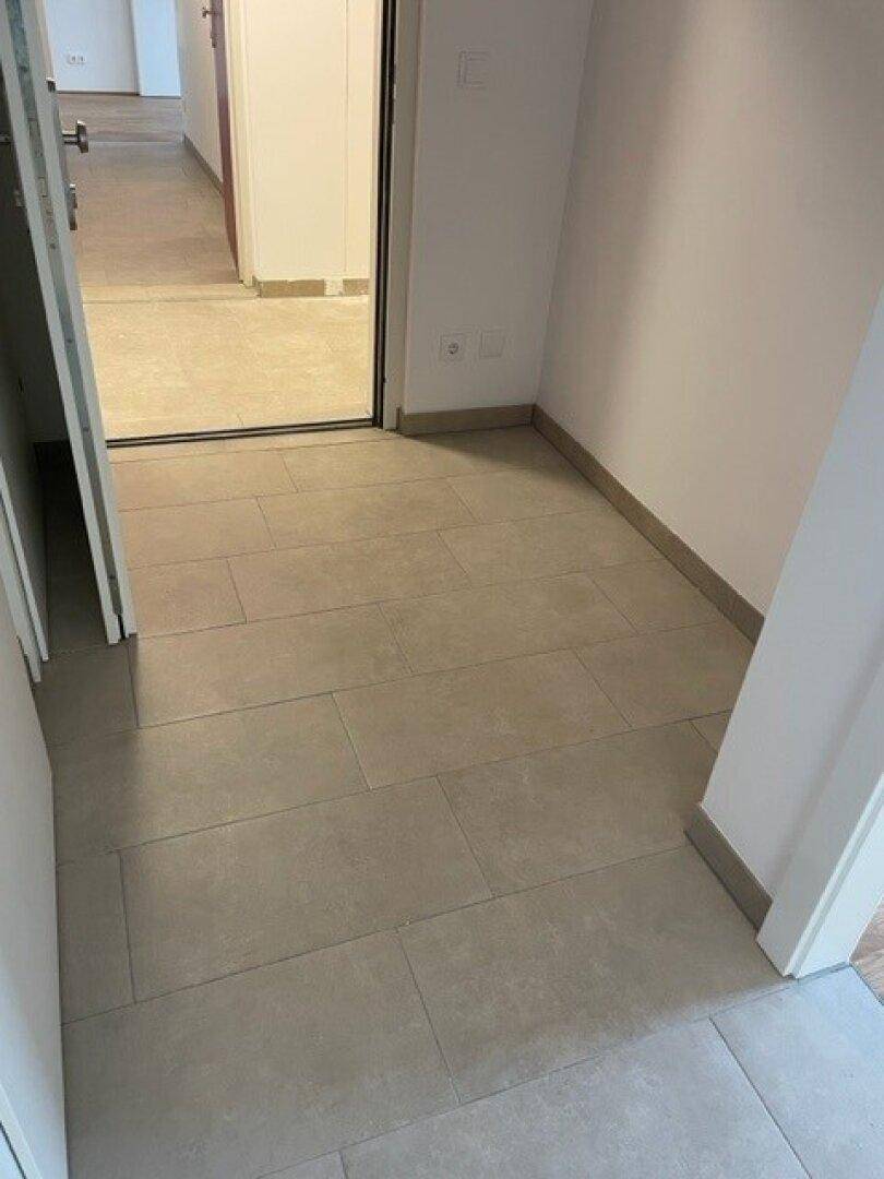 Eingangsbereich mit Fliesenboden und weiß gestrichenen Wänden, der zu den Wohnräumen führt.