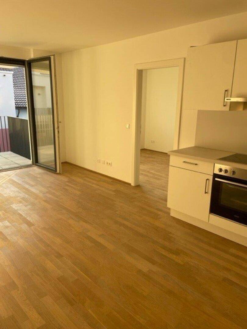 Offener Wohnbereich mit integrierter Küche und Zugang zu einem Balkon, durchflutet von Sonnenlicht.