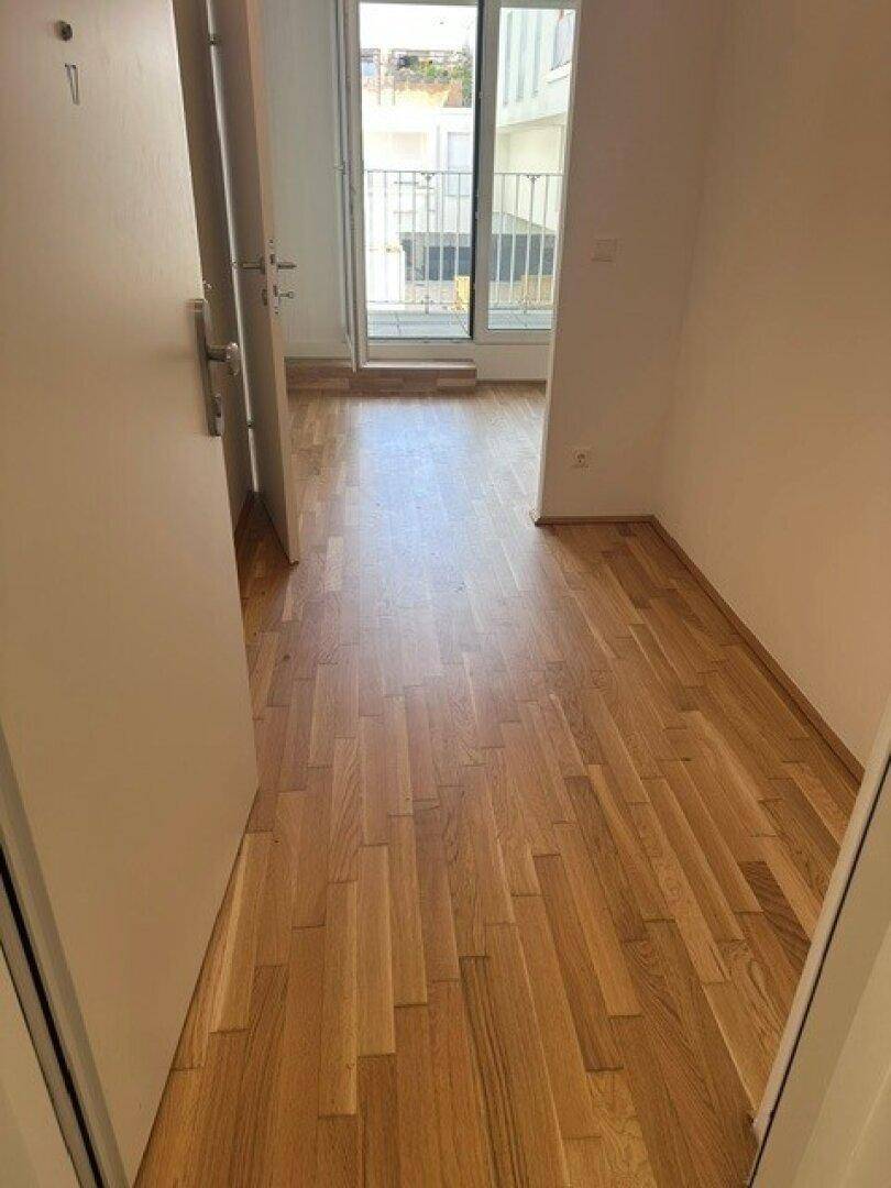 Langer Flur mit Parkettboden und Zugang zu einem Balkon oder einer Terrasse durch eine Glastür.