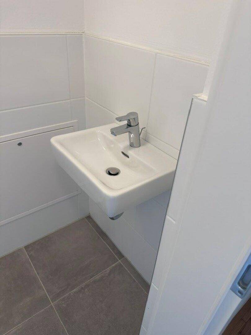 Kleines Gäste-WC mit wandmontiertem Waschbecken und modernen grauen Bodenfliesen.