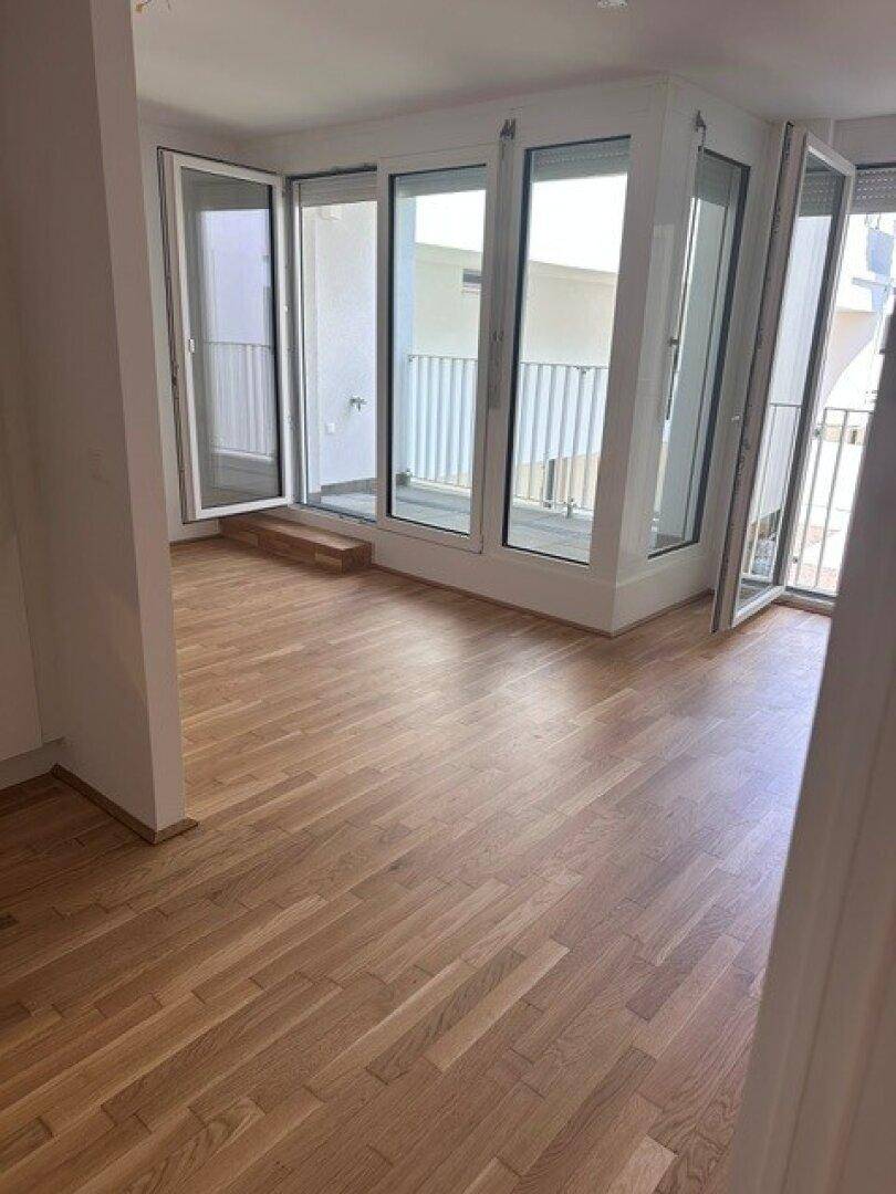 Heller Wohnbereich mit Parkettboden und mehreren Glastüren, die zu einem großzügigen Balkon führen.
