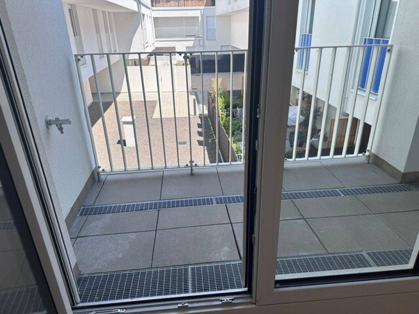 Balkon mit Fliesenboden und Metallgeländer, bietet Blick auf den ruhigen Innenhof.