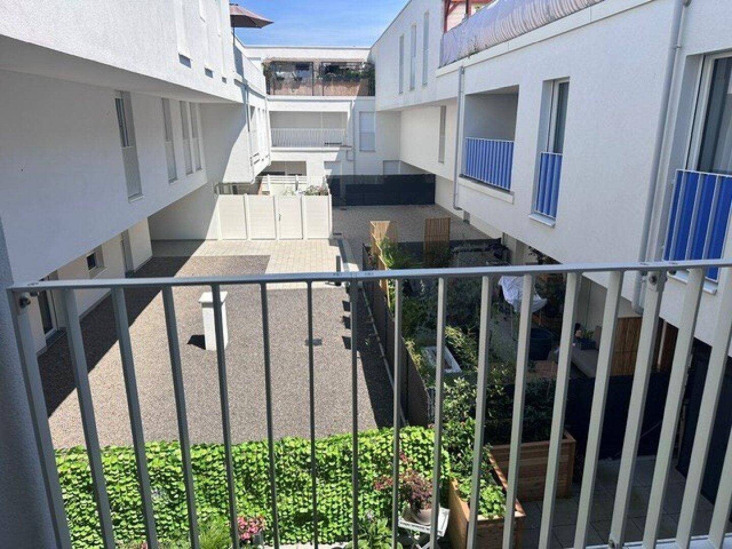 Blick vom Balkon auf einen begrünten Innenhof mit modernen Gebäudefassaden.