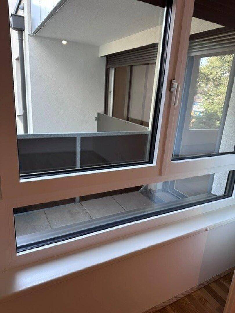 Blick aus dem Fenster auf einen angrenzenden Balkon oder Innenhofbereich mit weiteren Fenstern.