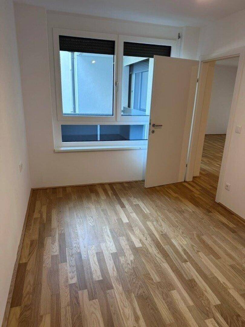 Helles Schlafzimmer mit Holzparkett und einem Fenster, das viel Tageslicht hereinlässt.
