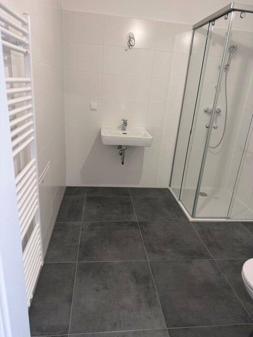 Modernes Badezimmer mit weiß gefliesten Wänden, Duschkabine und beheiztem Handtuchhalter.