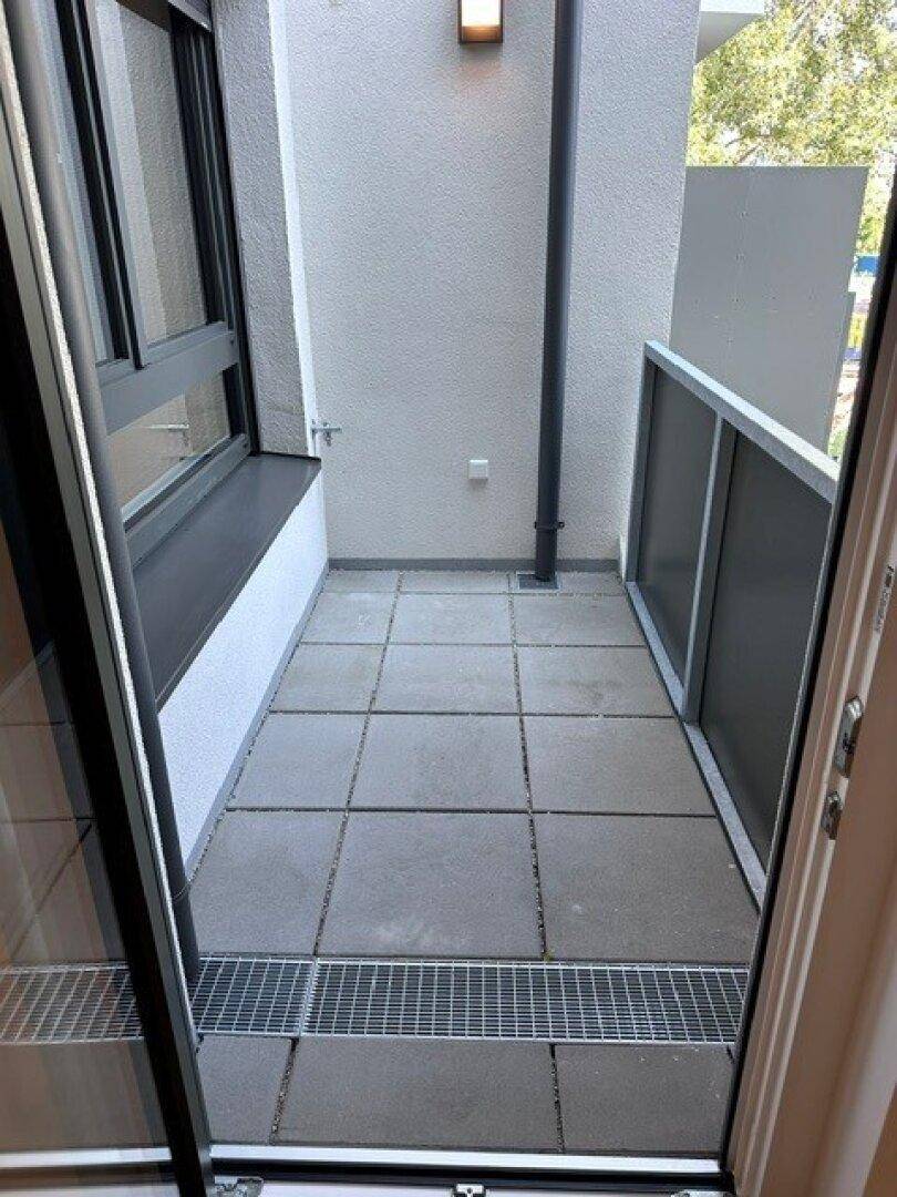 Kleiner Balkon mit grauen Fliesen und schlichtem Geländer, ideal für frische Luft.