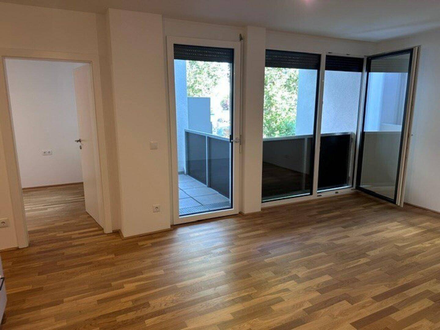 Heller Wohnbereich mit Holzparkett und großen Fenstertüren, die Zugang zum Balkon bieten.