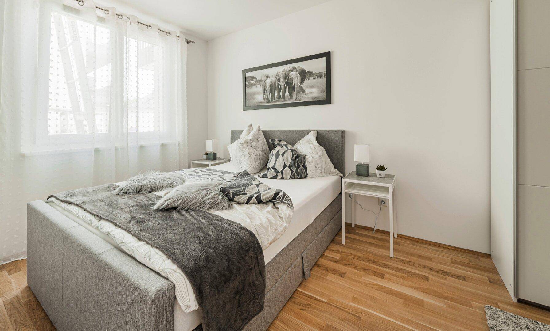 Gemütliches Schlafzimmer mit Doppelbett, Holzboden und großem Fenster für viel Tageslicht.
