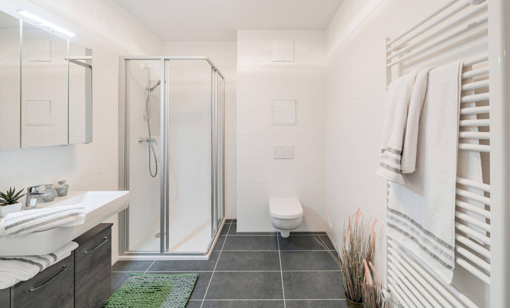 Modernes Badezimmer mit Duschkabine, Wand-WC, Einzelwaschbecken und beheiztem Handtuchhalter.