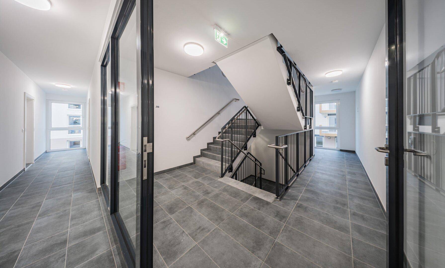 Helles Treppenhaus mit modernen Fliesen und Zugang zu den Wohneinheiten in einem Neubau.