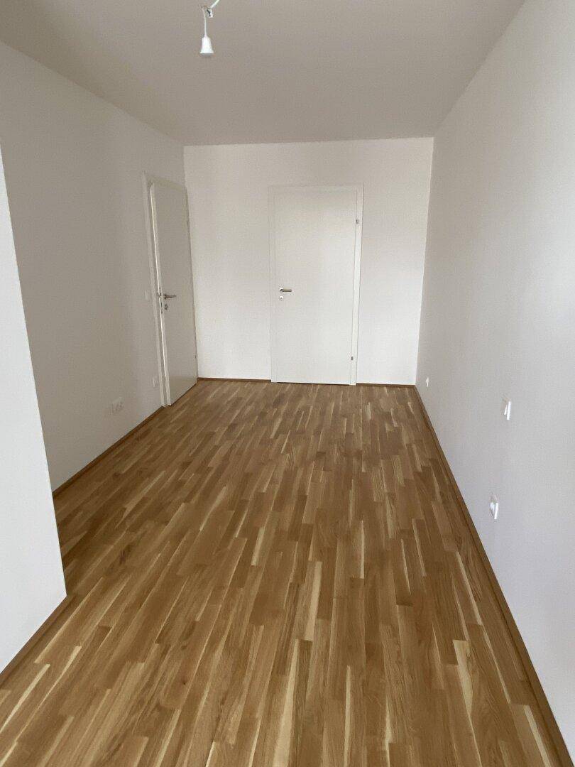 Weiteres helles Zimmer mit Holzboden und zwei Türen, vielseitig nutzbar als Schlaf- oder Arbeitszimmer.