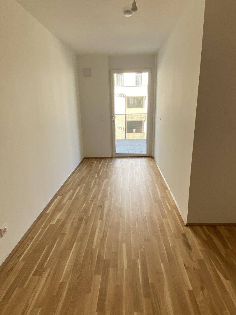 Helles Schlafzimmer mit Holzboden und Zugang zu einem Balkon, ideal für natürliche Belüftung.