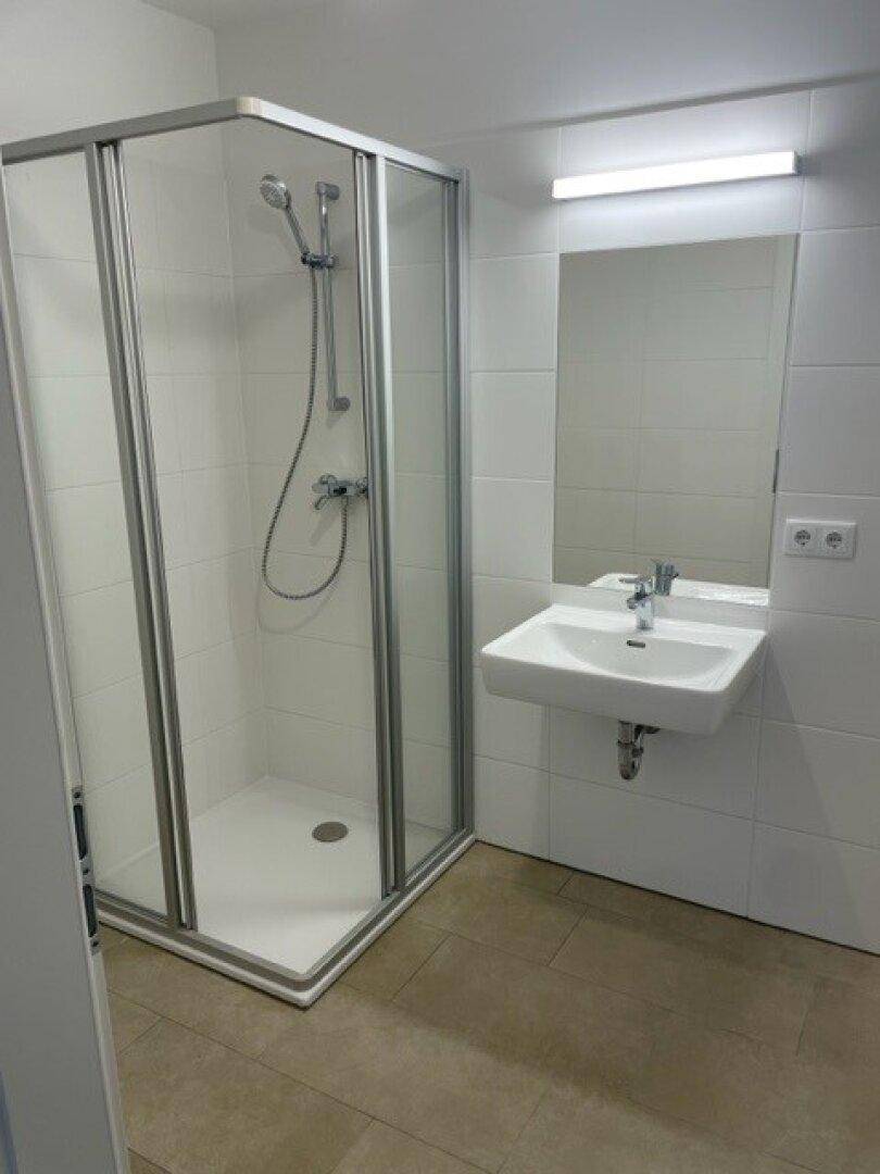 Helles Badezimmer mit Duschkabine, Waschbecken und weißen Wandfliesen.