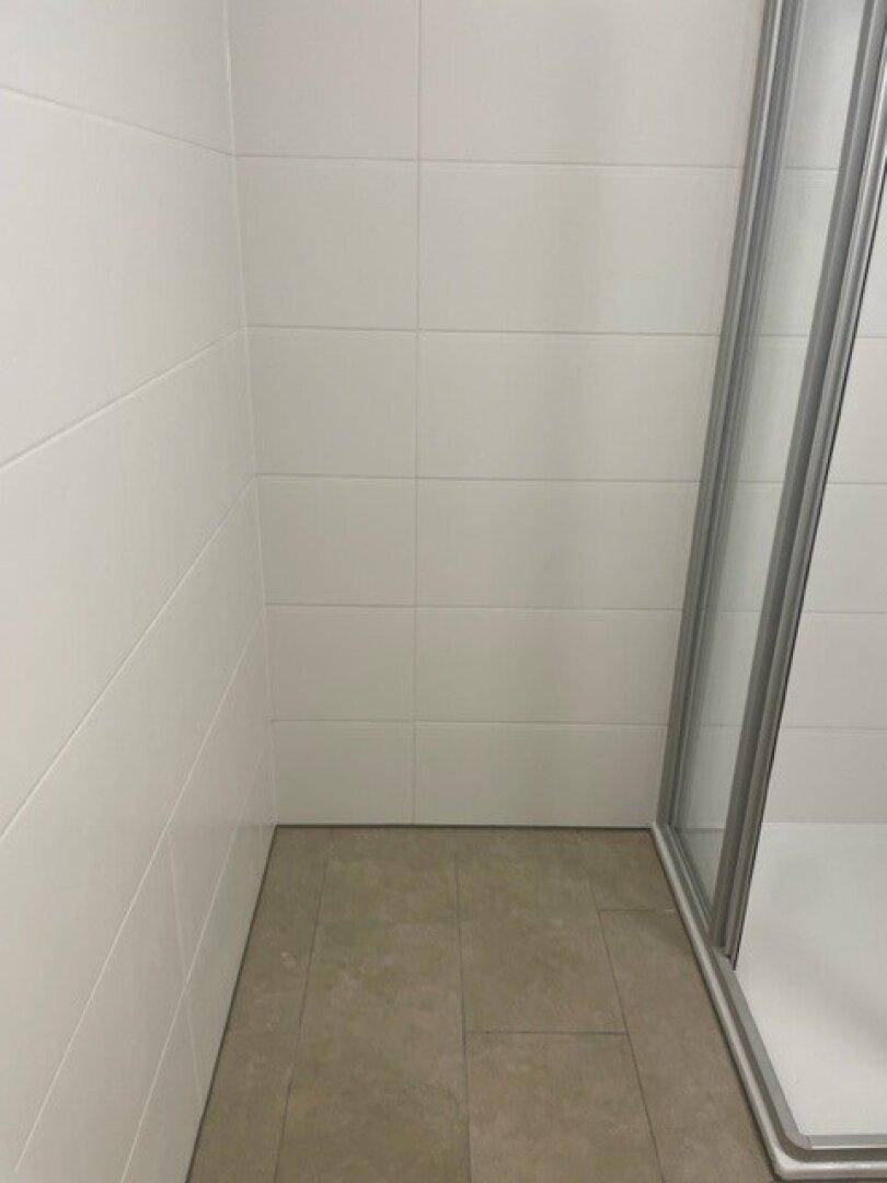 Sauber geflieste Ecke im Badezimmer mit hellen Wand- und Bodenfliesen.