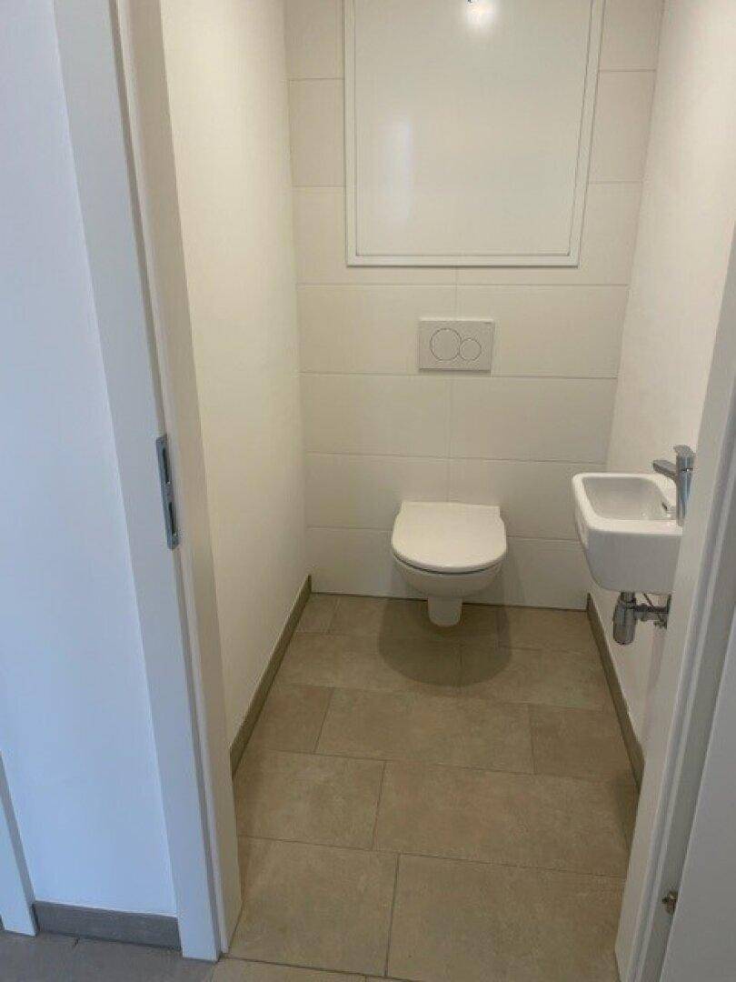 Modernes Gäste-WC mit wandhängendem WC, kleinem Waschbecken und Fliesenboden.