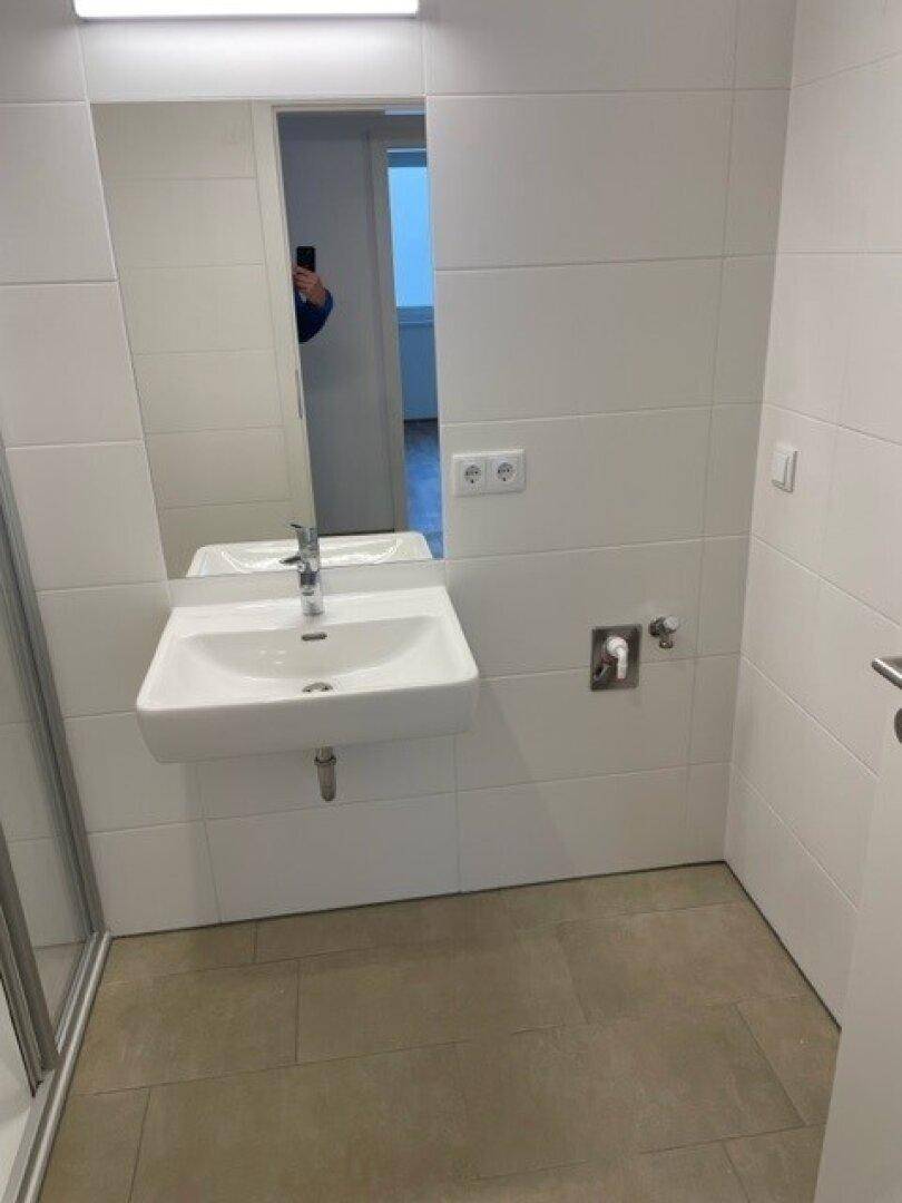 Waschbeckenbereich im Badezimmer mit großem Spiegel und weißen Wandfliesen.