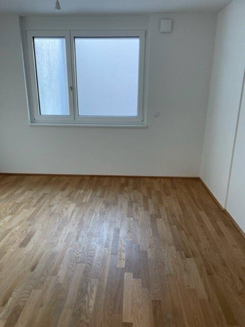 Helles Schlafzimmer mit Parkettboden und großem Fenster für viel Tageslicht.