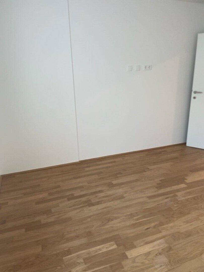 Geräumiges Schlafzimmer mit hellem Parkettboden und weißen Wänden.