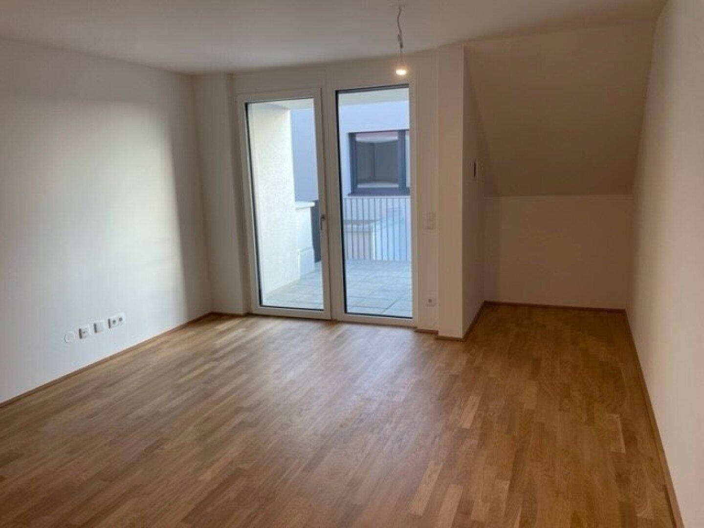 Heller Wohnbereich mit Parkettboden und Zugang zu einer großzügigen Terrasse.