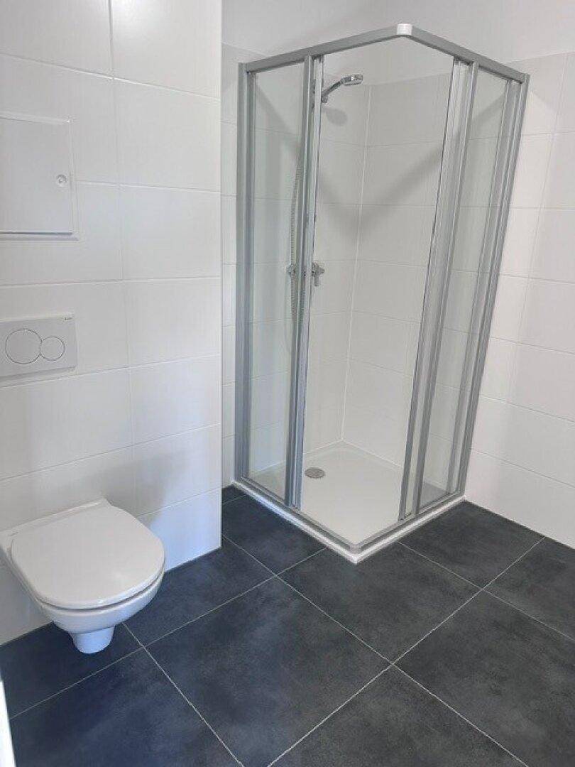 Modernes Badezimmer mit weiß gefliesten Wänden, dunklem Boden und einer Duschkabine.