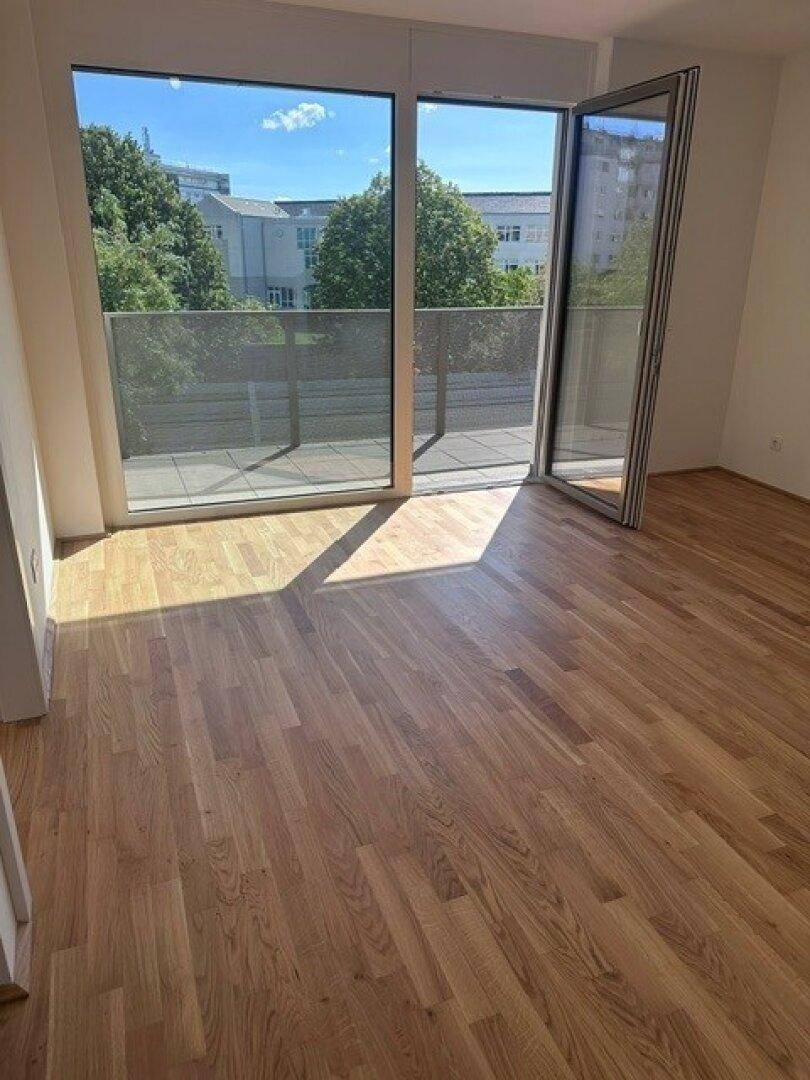 Lichtdurchfluteter Raum mit Holzboden und großem Fenster, das einen weiten Blick ins Grüne bietet.