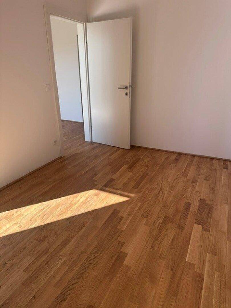 Leeres Zimmer mit Holzboden und einer Tür, die zu einem weiteren Raum führt.