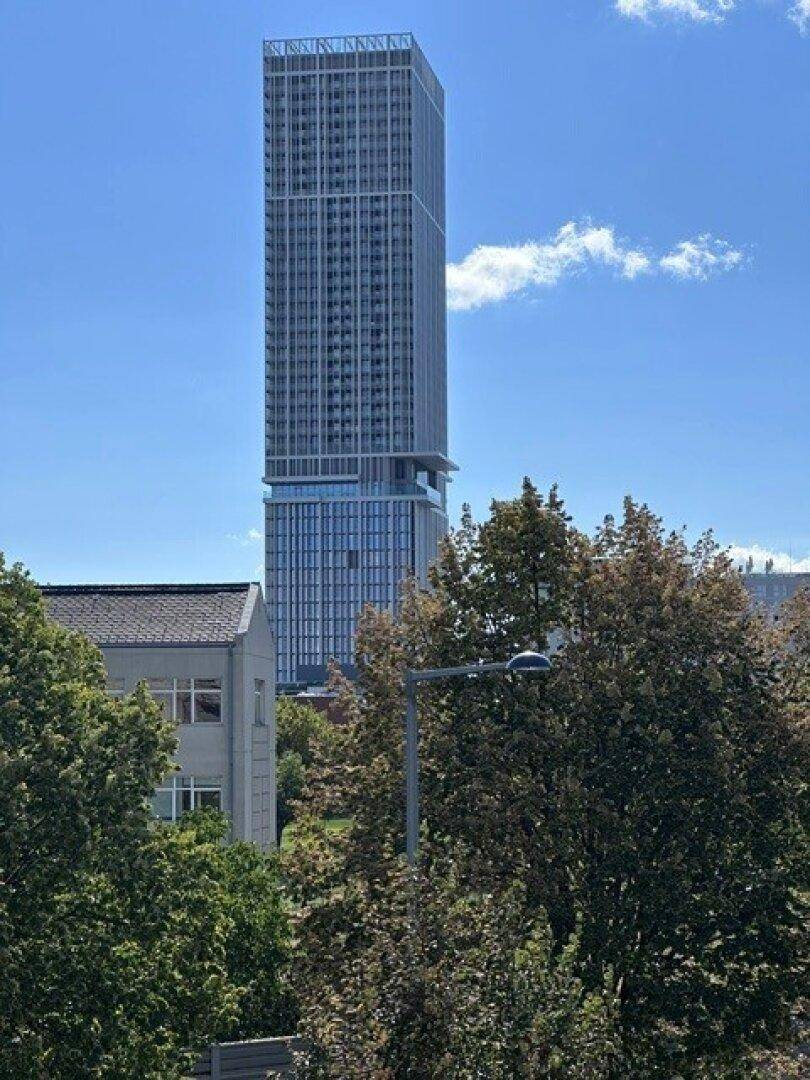 Hohes modernes Gebäude in der Ferne, umgeben von üppigem Grün unter blauem Himmel.