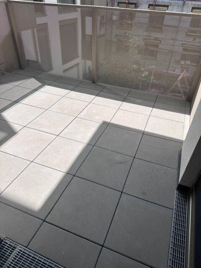 Heller Balkon mit grauen Fliesen und moderner Metallbrüstung, ideal zum Entspannen.