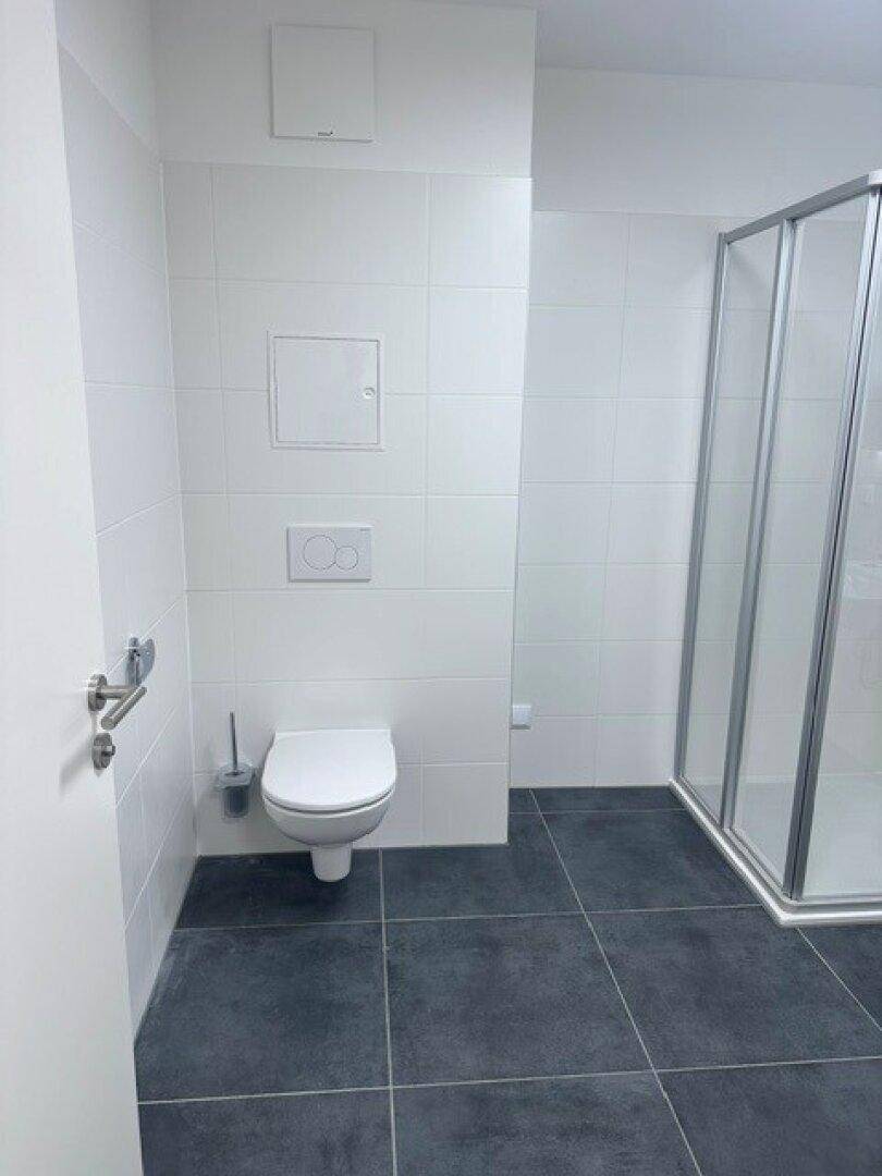 Modernes Badezimmer mit weißen Wandfliesen, dunklen Bodenfliesen und einer Duschkabine.