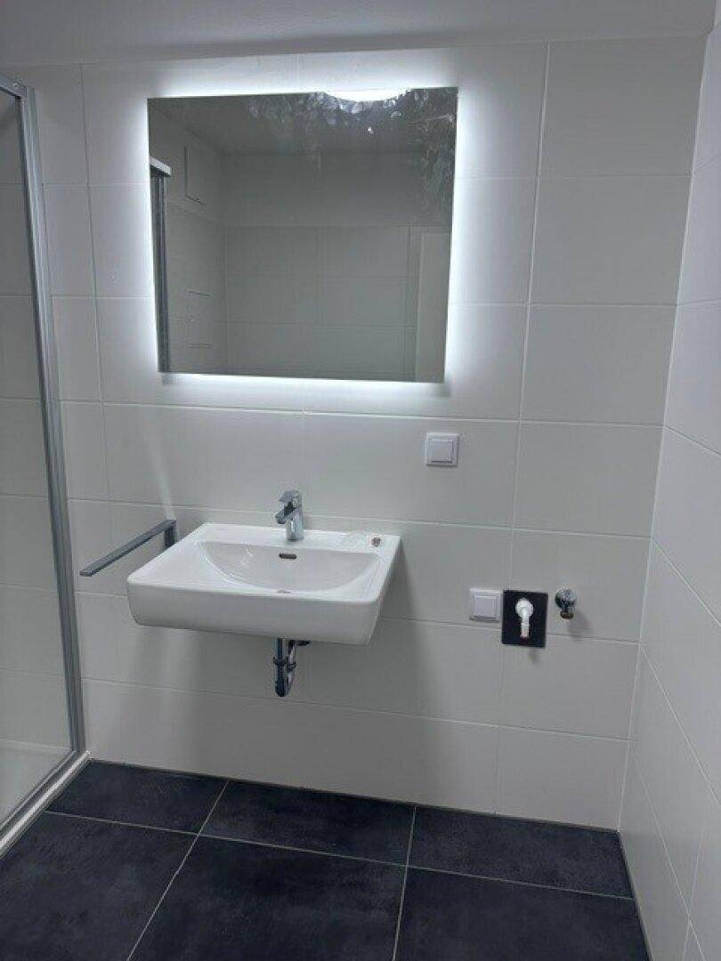 Detailansicht des wandhängenden Waschbeckens mit beleuchtetem Spiegel im modernen Bad.