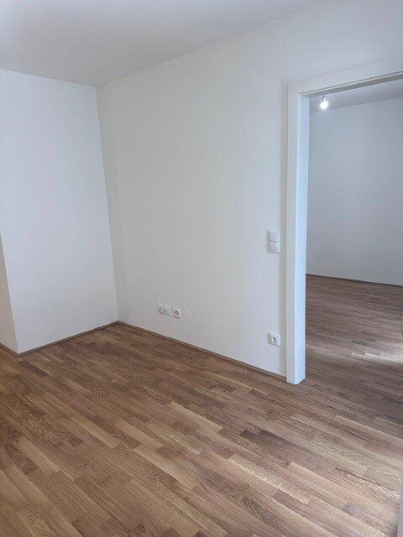 Leerer Raum mit hellem Parkettboden und weißen Wänden, bereit zur individuellen Gestaltung.