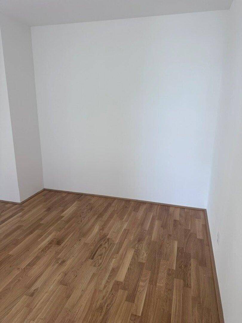 Leerer Raum mit hellem Parkettboden und weißen Wänden, ideal für Schlaf- oder Arbeitszimmer.