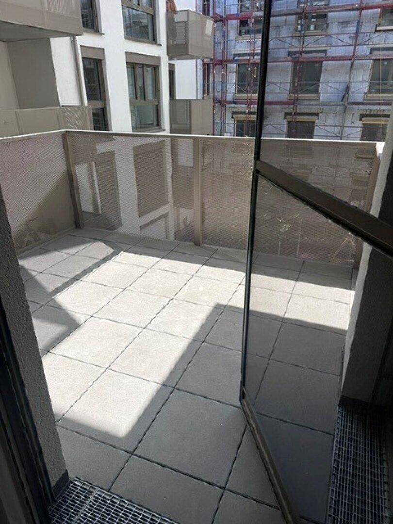 Geräumiger Balkon mit hellen Fliesen und moderner Brüstung, umgeben von Neubauten.