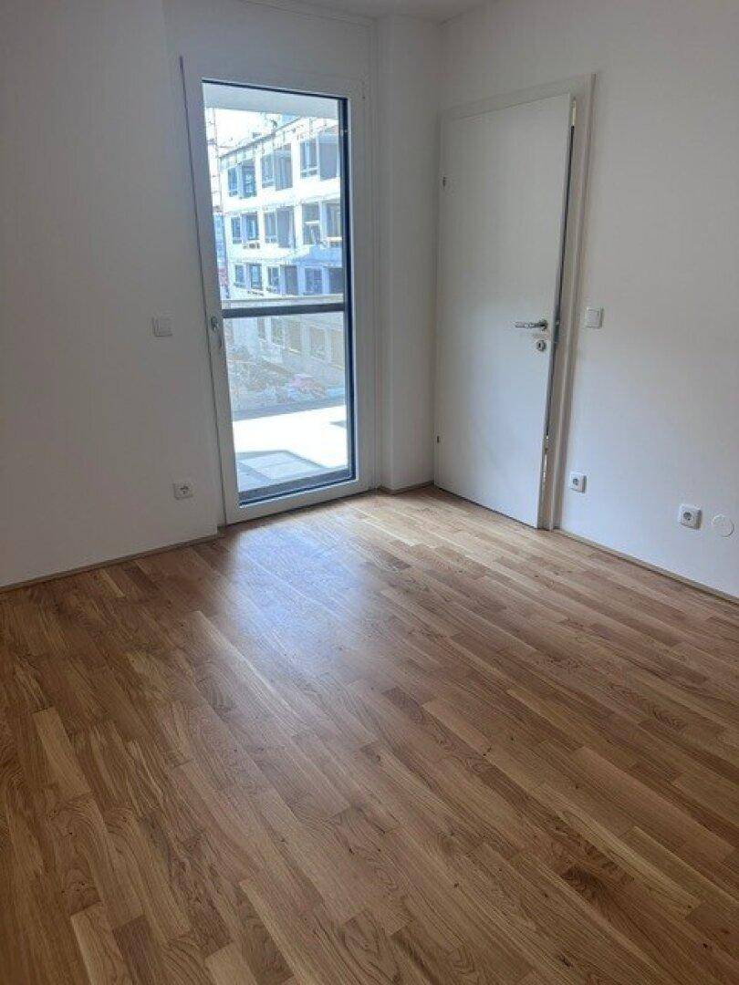 Heller Raum mit Parkettboden und Tür zum Außenbereich, bietet viel Tageslicht.