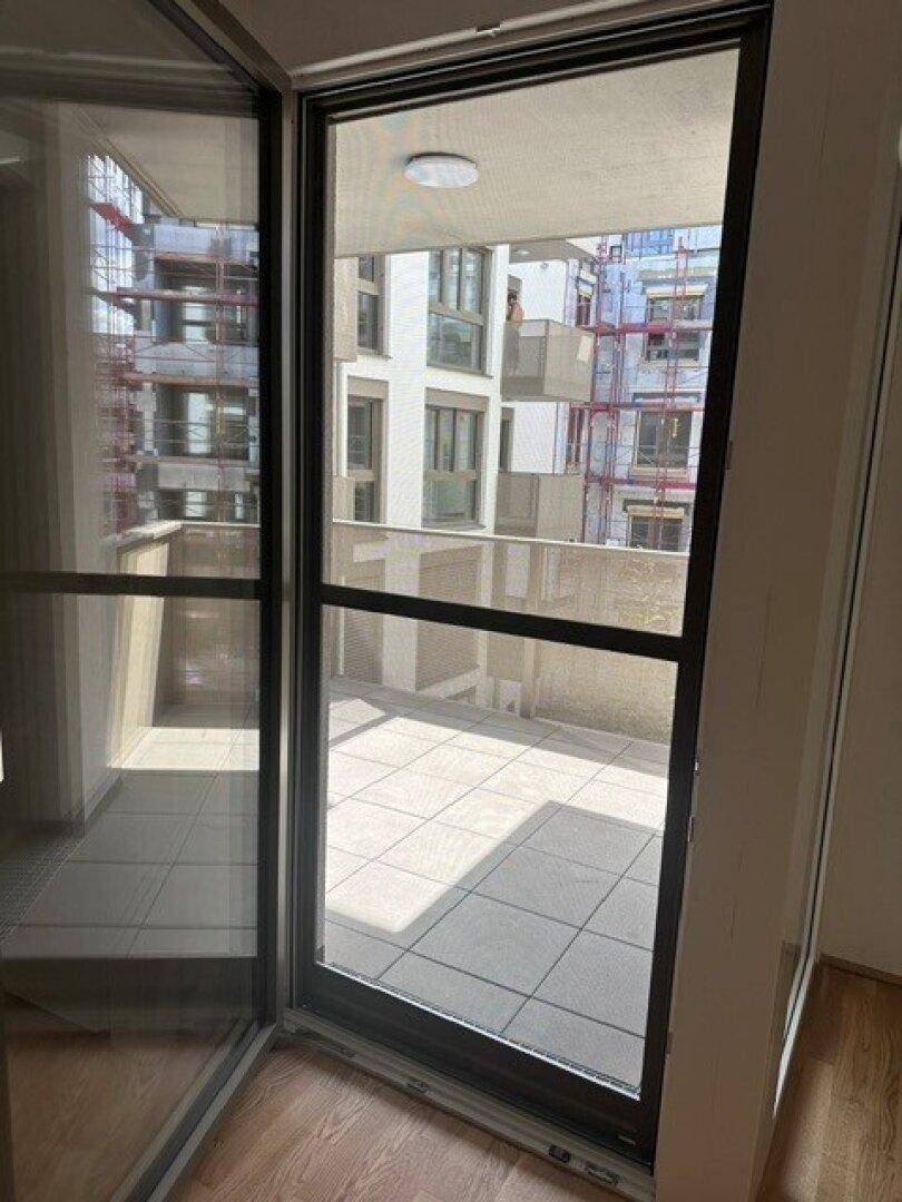 Blick vom Innenraum auf den gefliesten Balkon mit umliegenden Gebäuden und Baustelle.