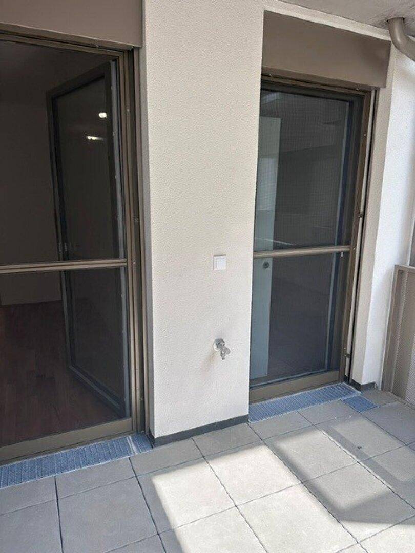 Zugang zum gefliesten Balkon durch zwei große Glastüren mit Rollläden.