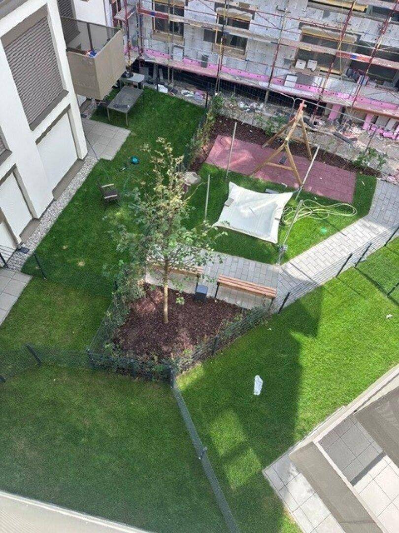 Gemeinschaftsgarten mit Rasenflächen, Bäumen und einem kleinen Spielbereich.