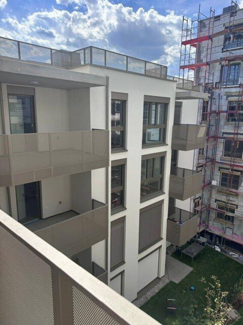 Moderne Gebäudefassade mit Balkonen und großen Fenstern, umgeben von Baustellen.