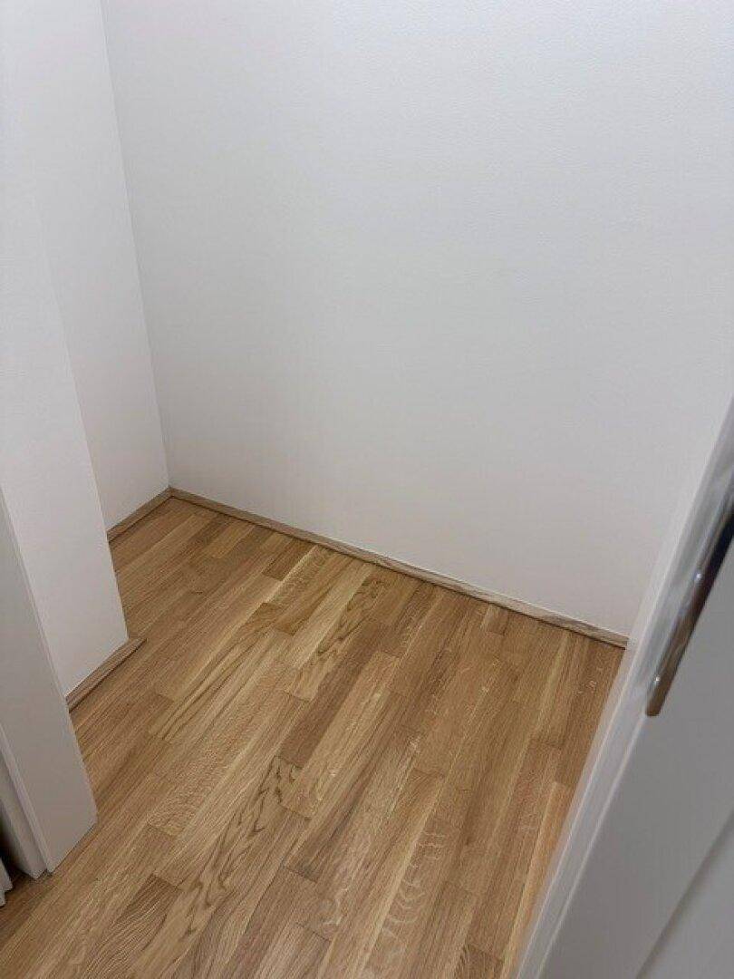 Leerer Abstellraum mit hellem Holzboden und weißen Wänden, bereit zur Nutzung.