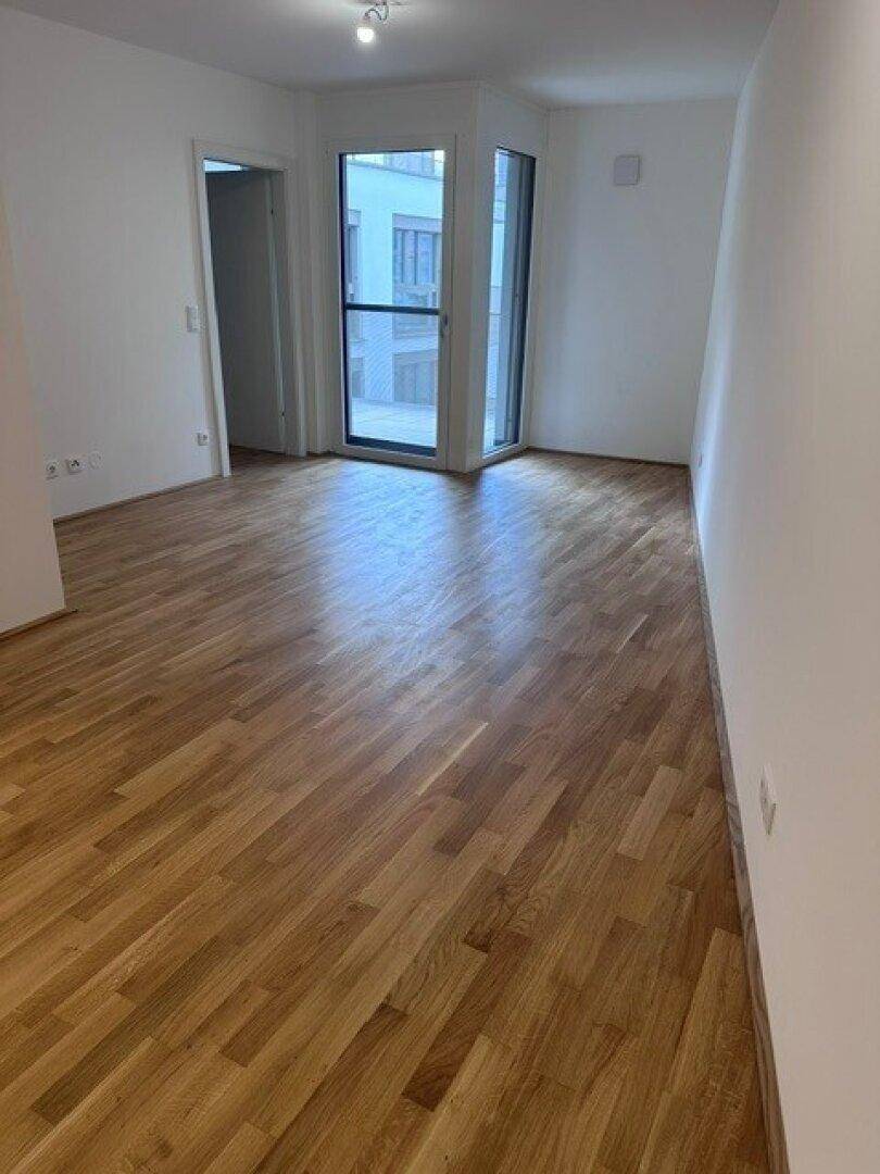 Heller Wohnraum mit großen Fenstern und Zugang zu einem Außenbereich, ausgestattet mit Parkettboden.