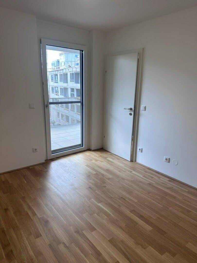 Helles Zimmer mit Holzboden und großem Fenster, das viel Tageslicht hereinlässt.