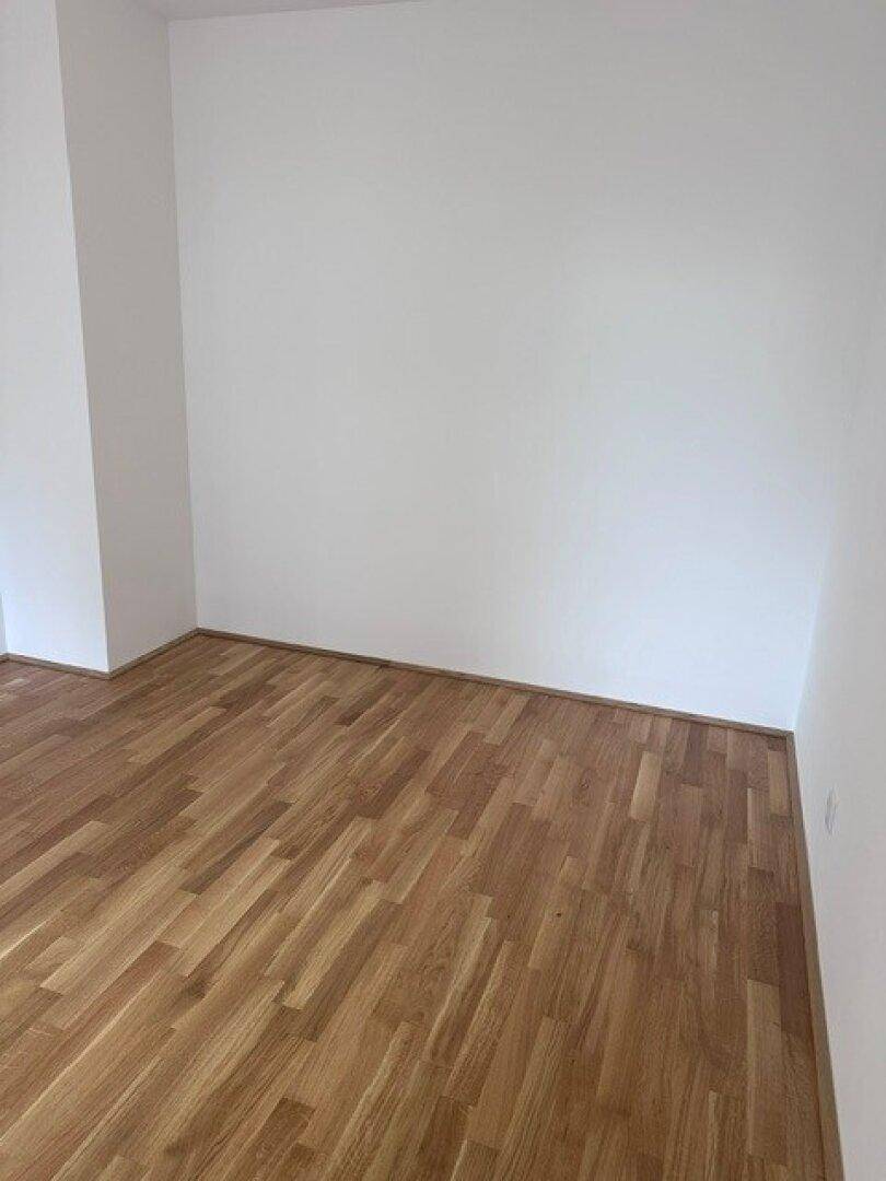 Leeres Zimmer mit hellem Parkettboden und weißen Wänden, bereit zur individuellen Gestaltung.