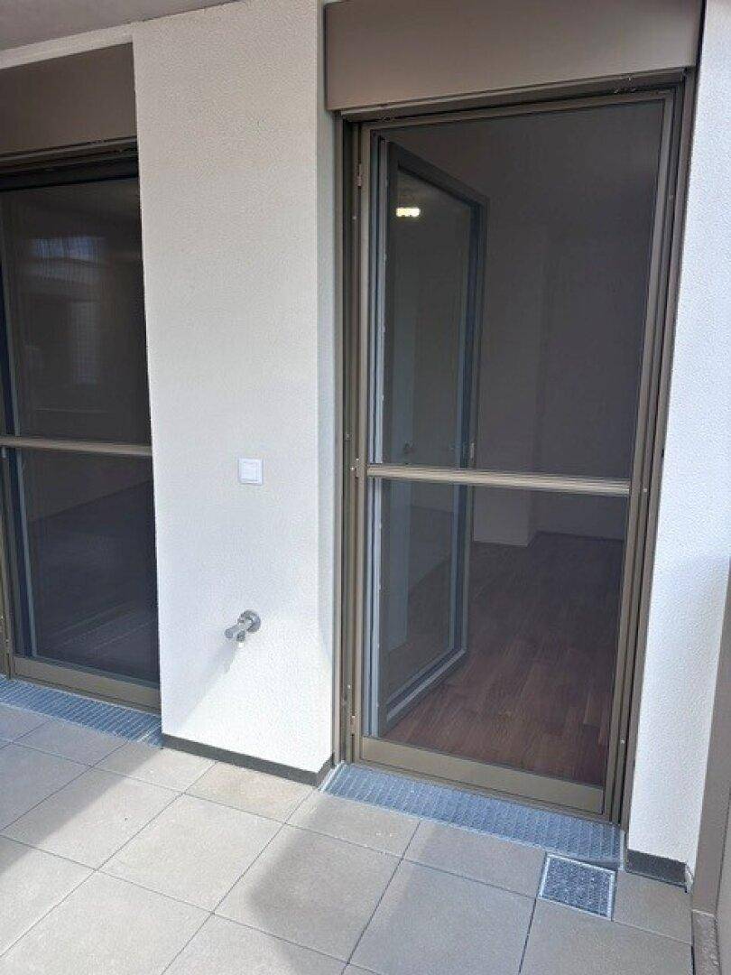 Balkon mit Fliesenboden und Rollläden, der Zugang zu den Innenräumen bietet.